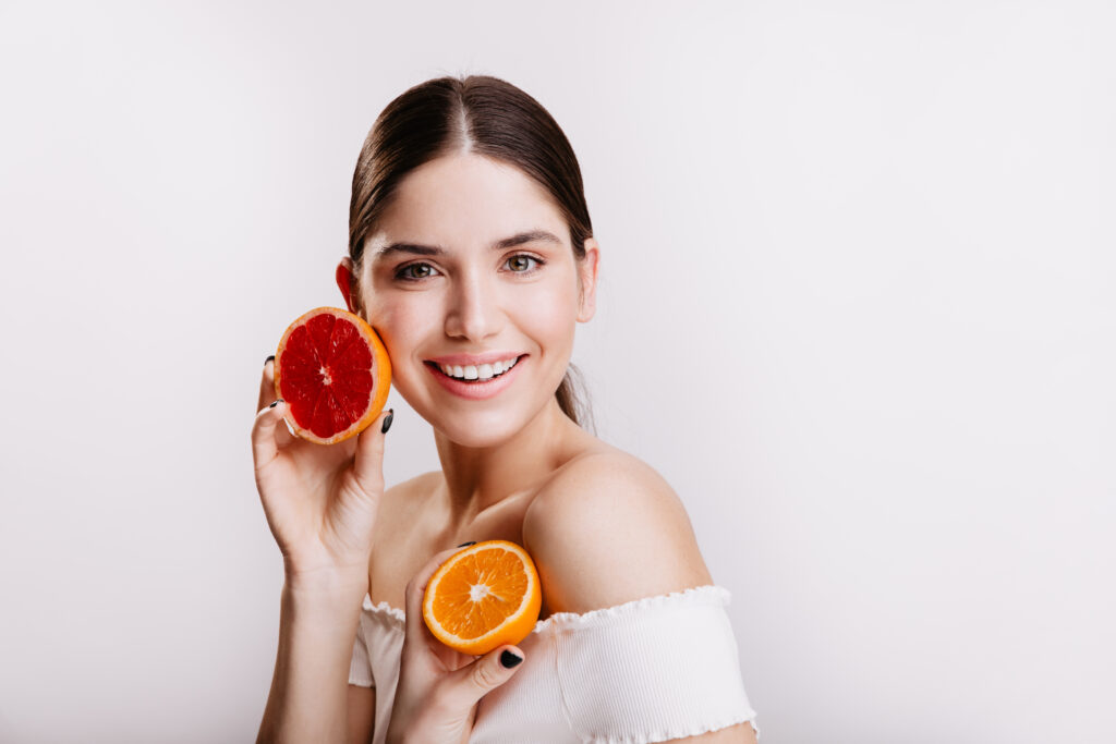lady with green eyes in white top posing on isolated background without filters and makeup. woman holds orange and grapefruit near face. lady with green eyes in white top posing on isolated background without filters and makeup. woman holds orange and grapefruit near face.